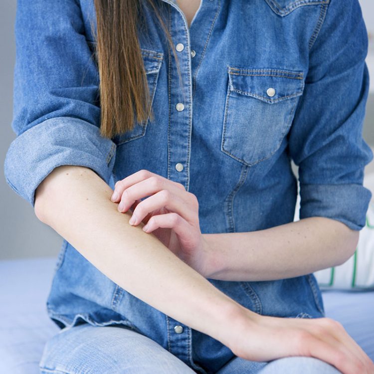 A woman scratching at her arm wearing a denim shirt