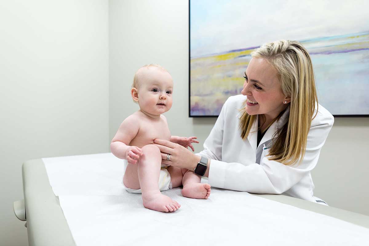 A doctor with a baby both smiling and looking at the camera.